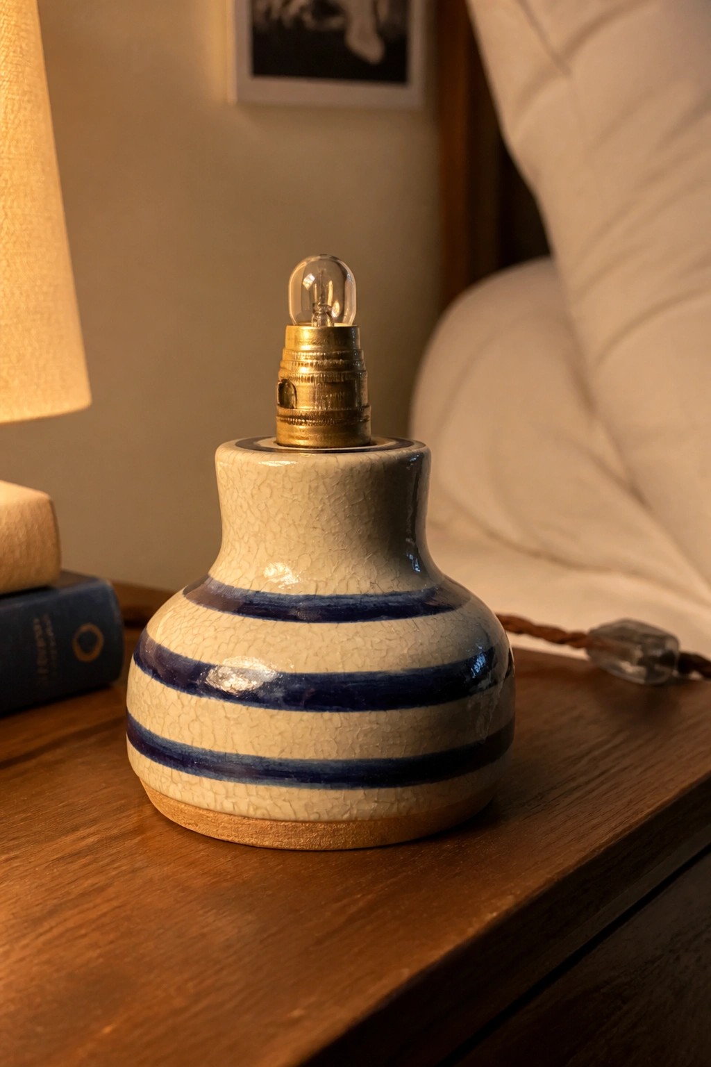 Blue-striped crackled ceramic lamp base with exposed bulb on wooden nightstand