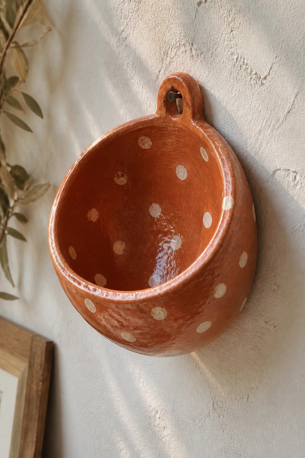 Hanging orange terracotta bowl with white polka dots on textured wall