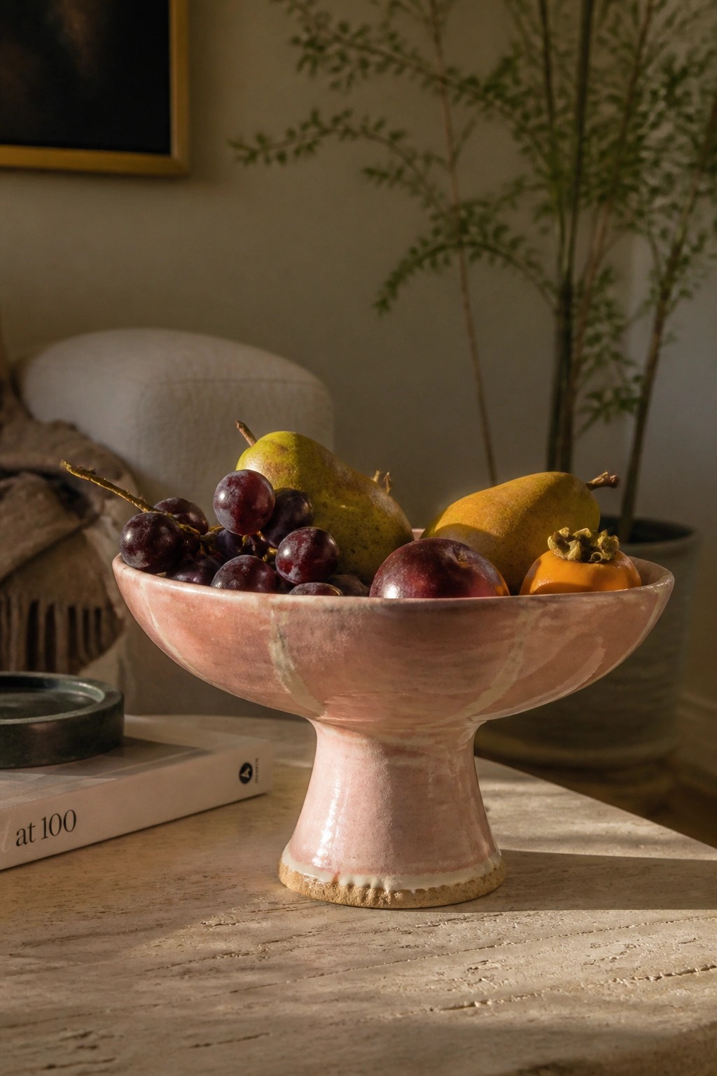 Pink pedestal bowl with grapes, pears, plum and persimmon on wooden table