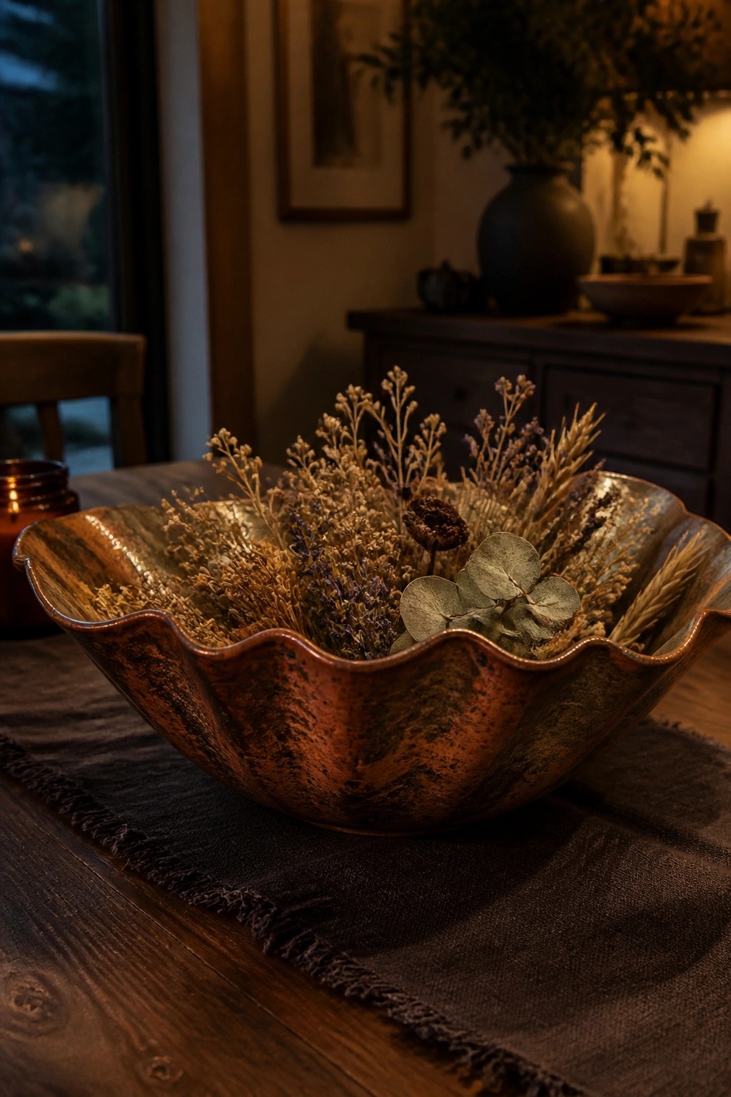 Hammered copper bowl brimming with dried wildflowers and eucalyptus on wooden table.