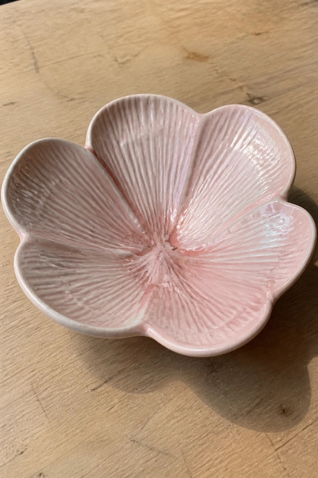 Pink ceramic flower-shaped bowl with ribbed interior on wooden surface.