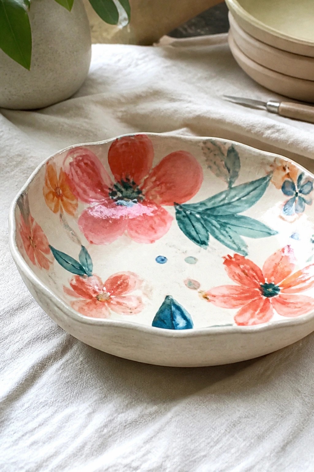 White ceramic bowl with red and pink watercolor flowers on linen cloth.