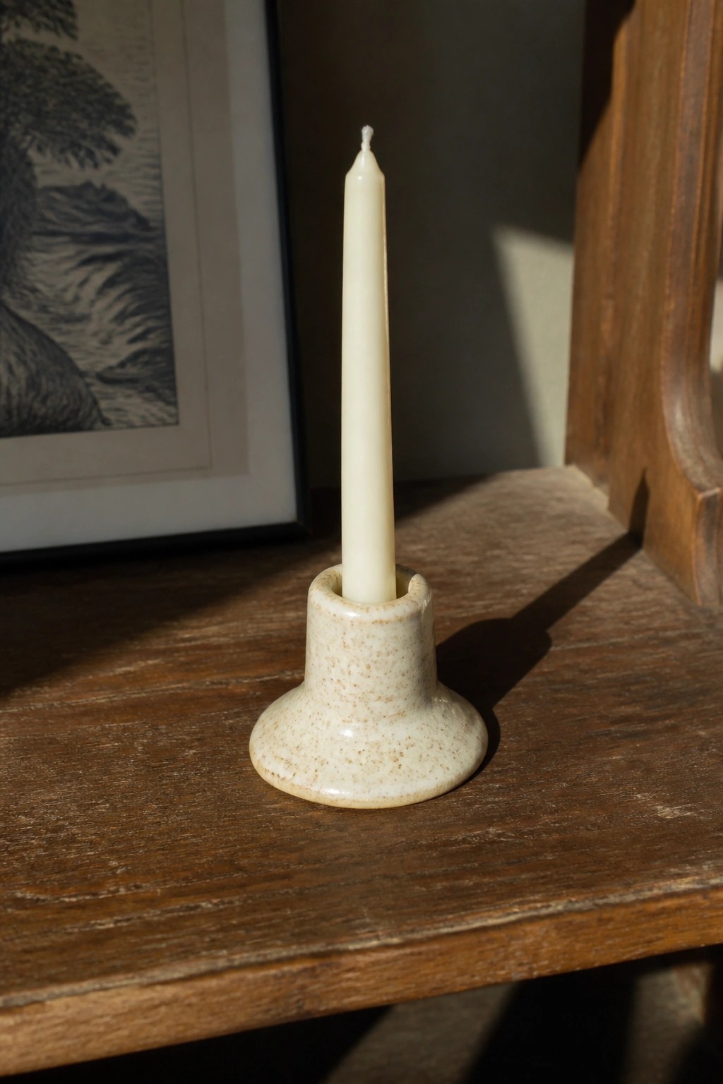 White candle in speckled ceramic holder on wooden table in sunlight