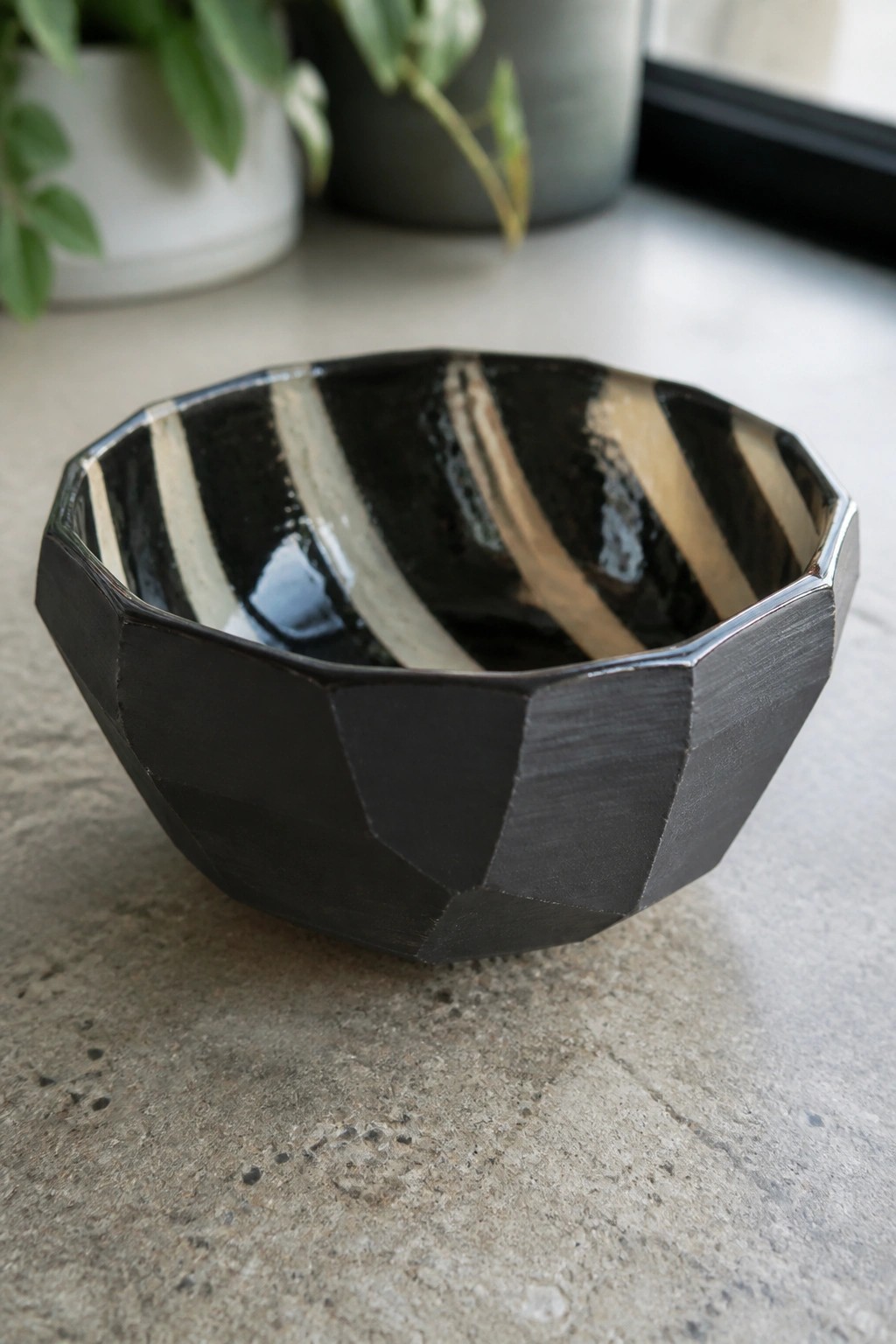 Faceted black ceramic bowl with striped interior on gray concrete surface