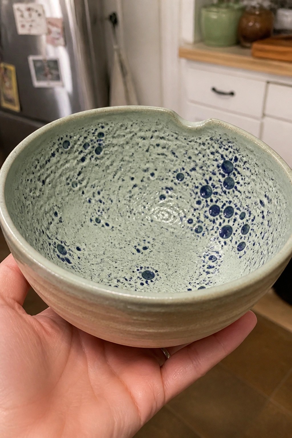 Hand holds light green ceramic bowl with blue speckles and notched rim.