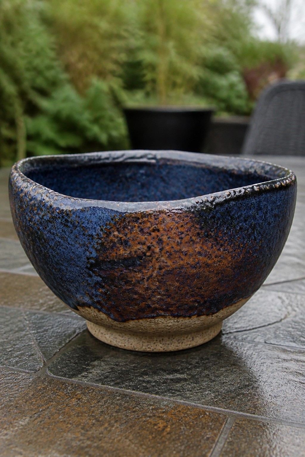 Ceramic bowl with blue-brown speckled glaze on wet stone table outdoors