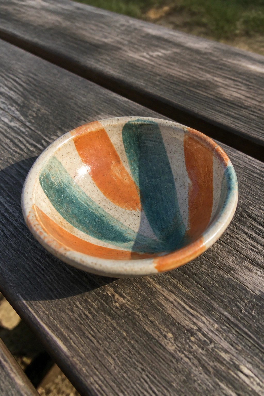 Small colorful ceramic bowl with orange and teal stripes on wooden table