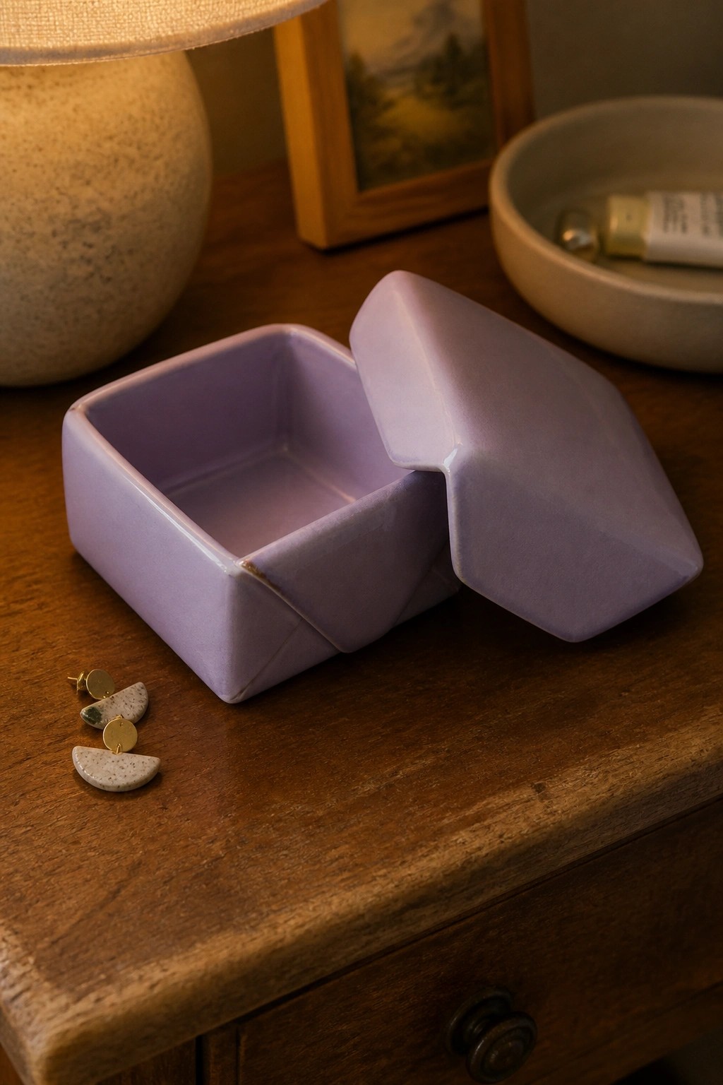 Open lavender ceramic box on wooden table with gold earrings beside it