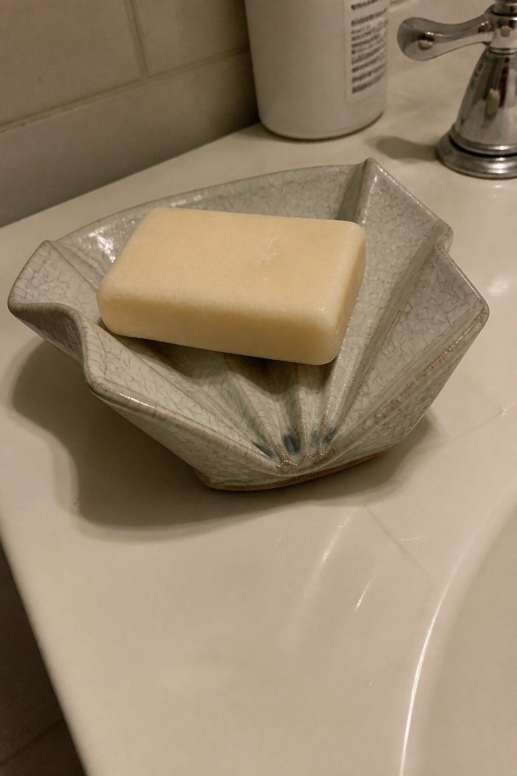 Pale yellow soap bar in scalloped crackle-glaze ceramic dish on white sink