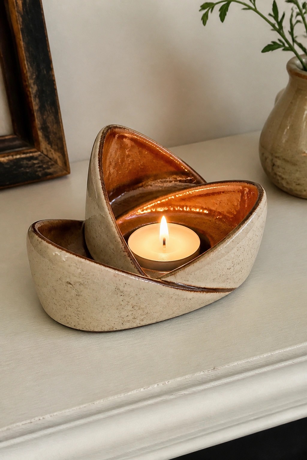 Lit candle in abstract beige ceramic holder with glossy brown interior