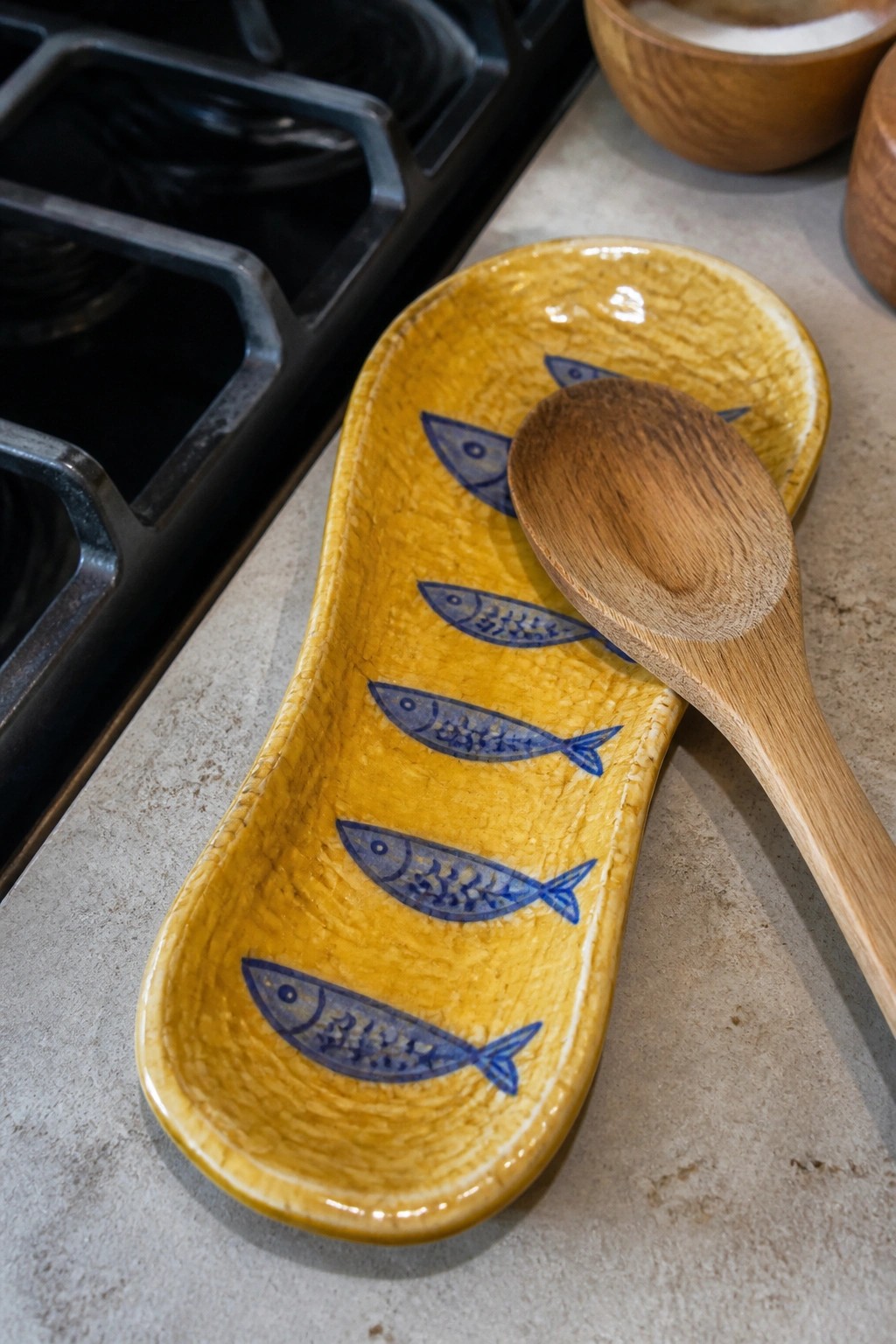 Yellow ceramic dish with blue fish designs and wooden spoon on counter