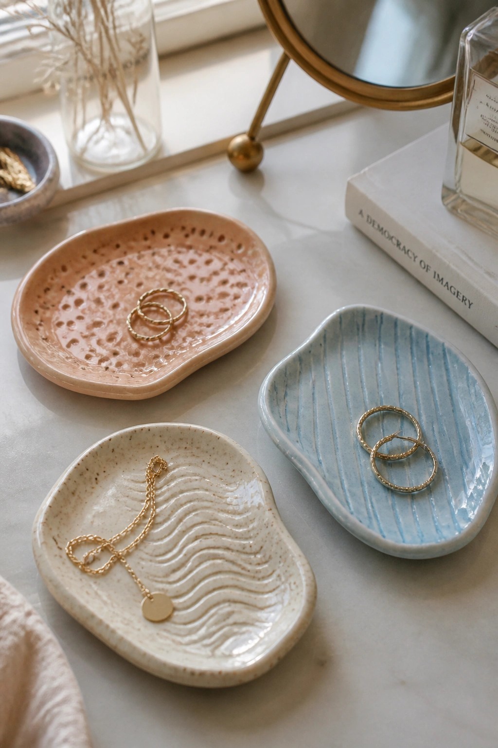 Three ceramic trays holding gold jewelry on marble vanity surface.