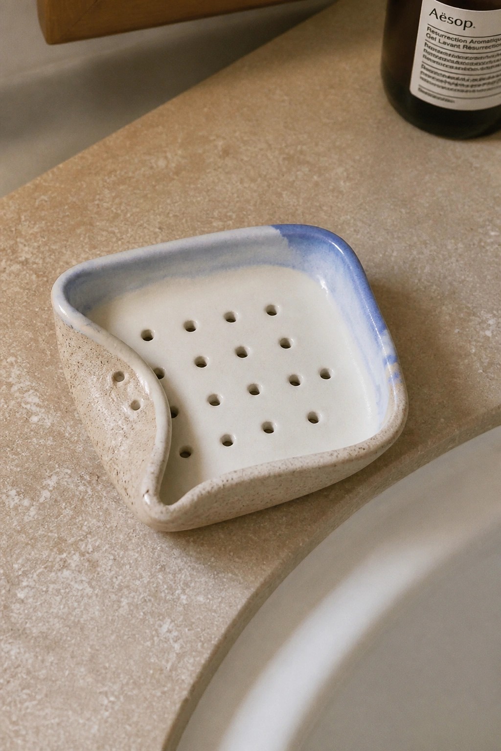 Speckled ceramic soap dish with blue rim on beige bathroom countertop near sink