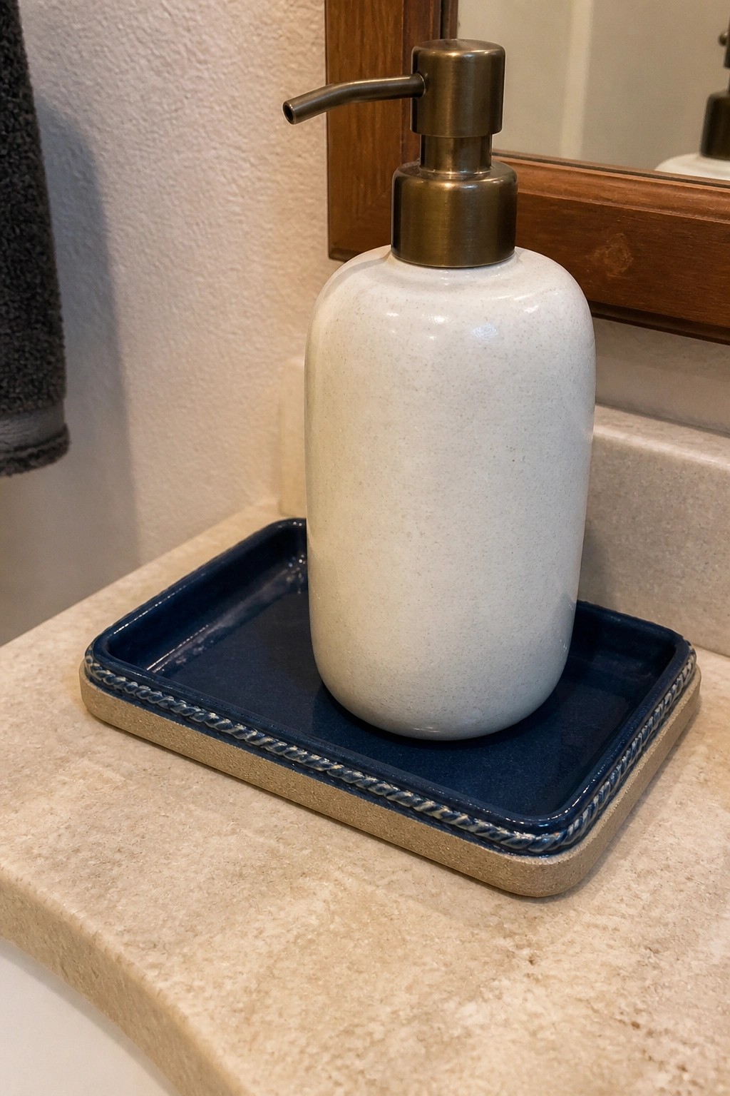 White ceramic soap dispenser with bronze pump on blue tray atop marble counter