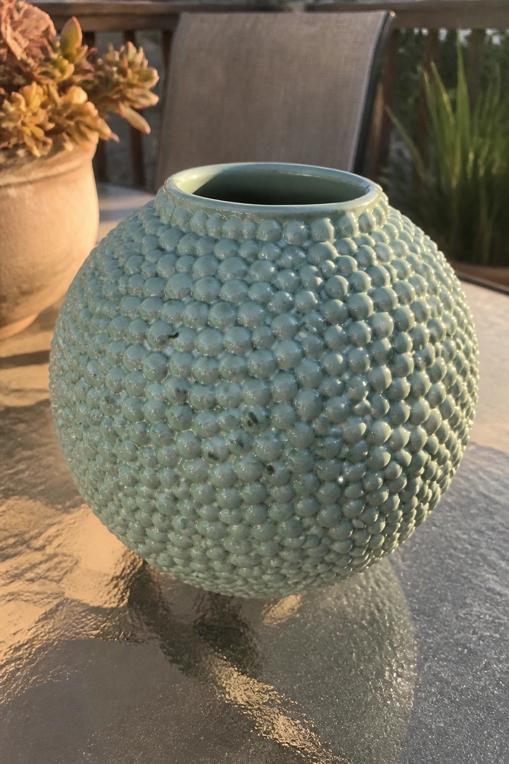 Mint green bumpy ceramic vase on reflective glass table outdoors