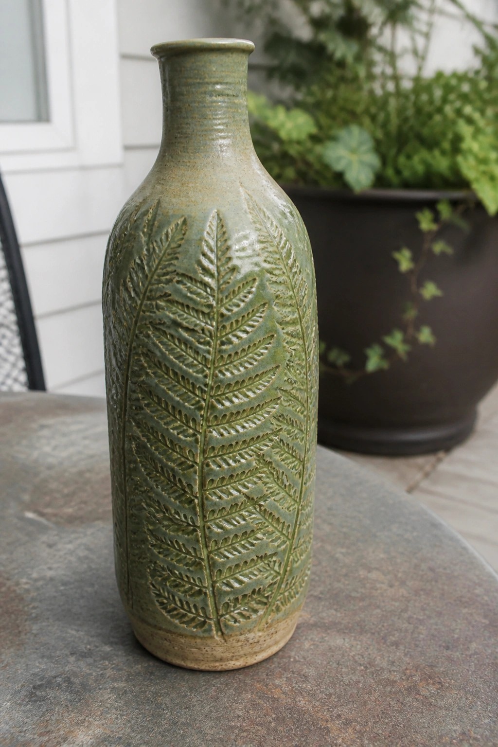 Green ceramic vase with embossed fern leaves on stone table outdoors