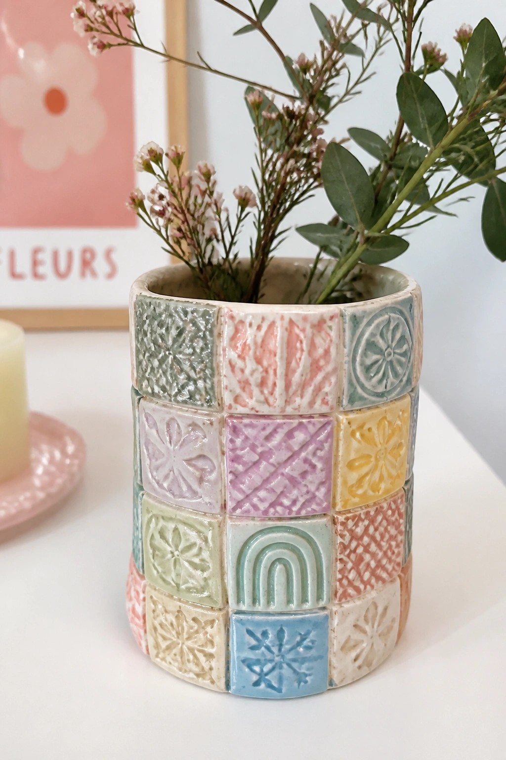 Colorful patchwork ceramic vase with embossed patterns holding green foliage and pink flowers