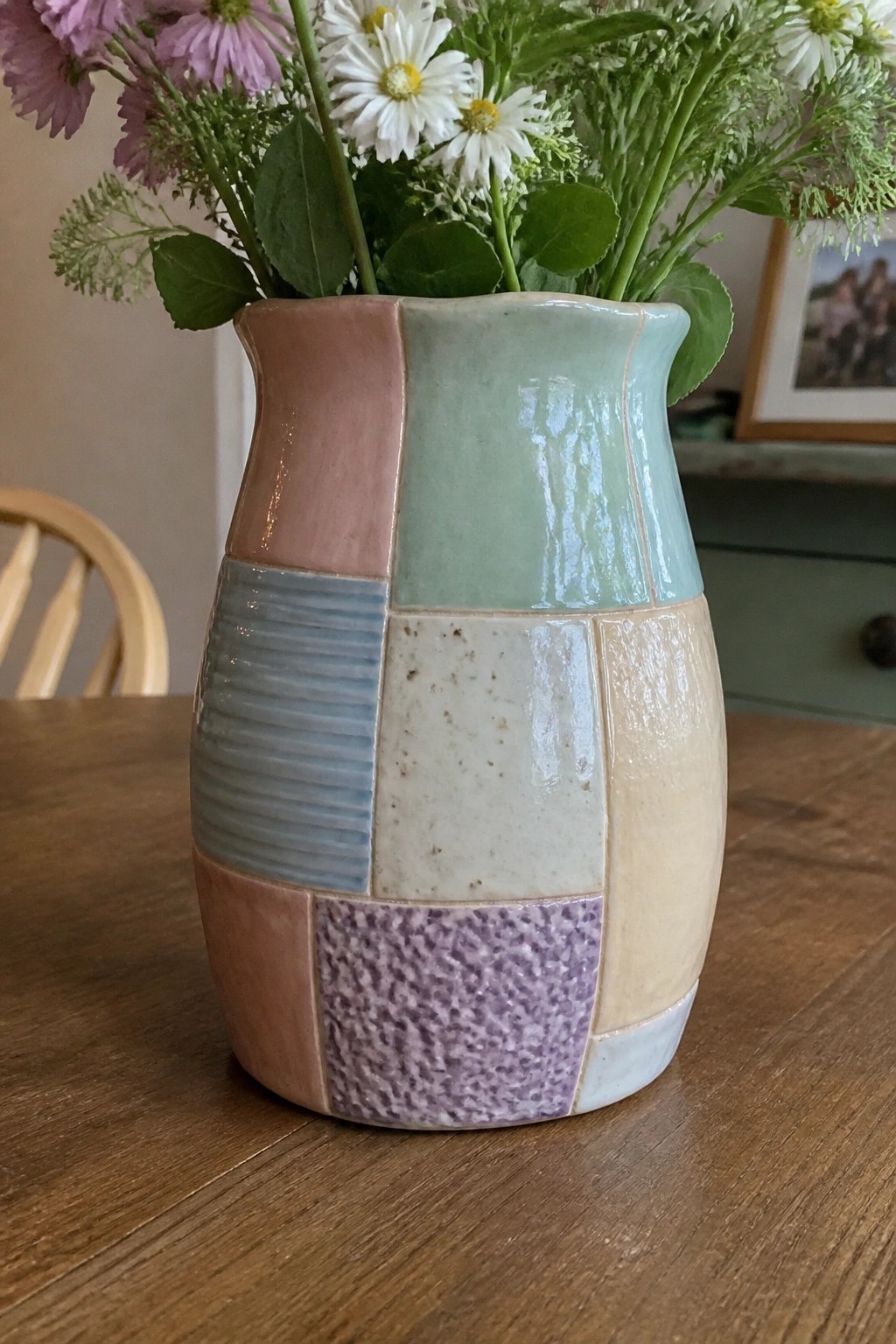 Colorful patchwork ceramic vase with pink, green, and purple sections holding flowers on wooden table