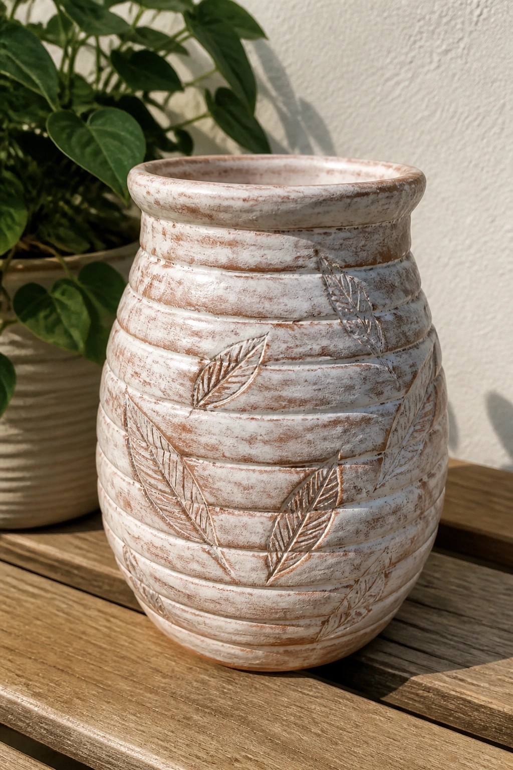 White ridged ceramic vase with leaf imprints on wooden table.