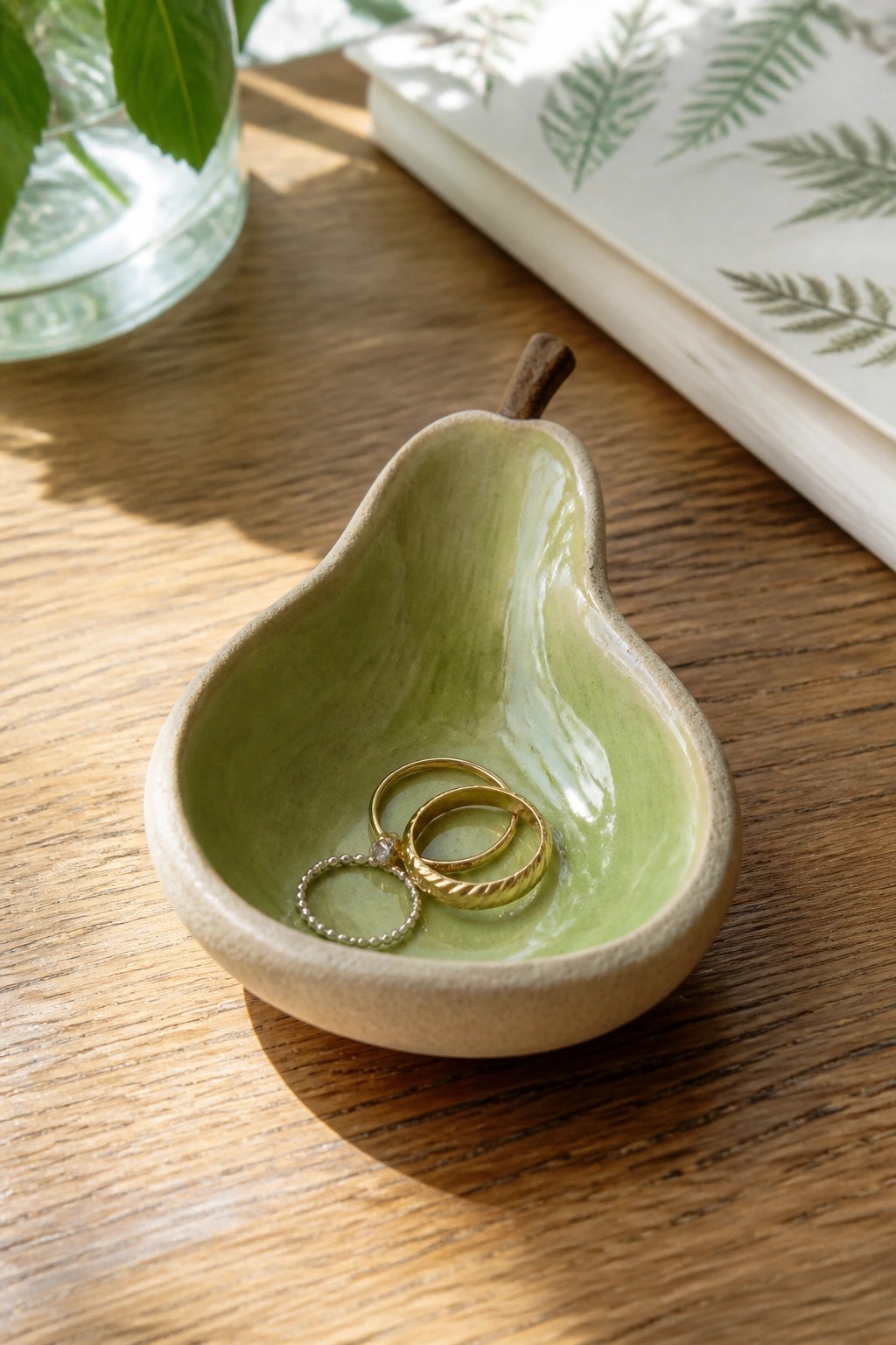 Green pear-shaped ceramic dish holding gold and silver rings on wood