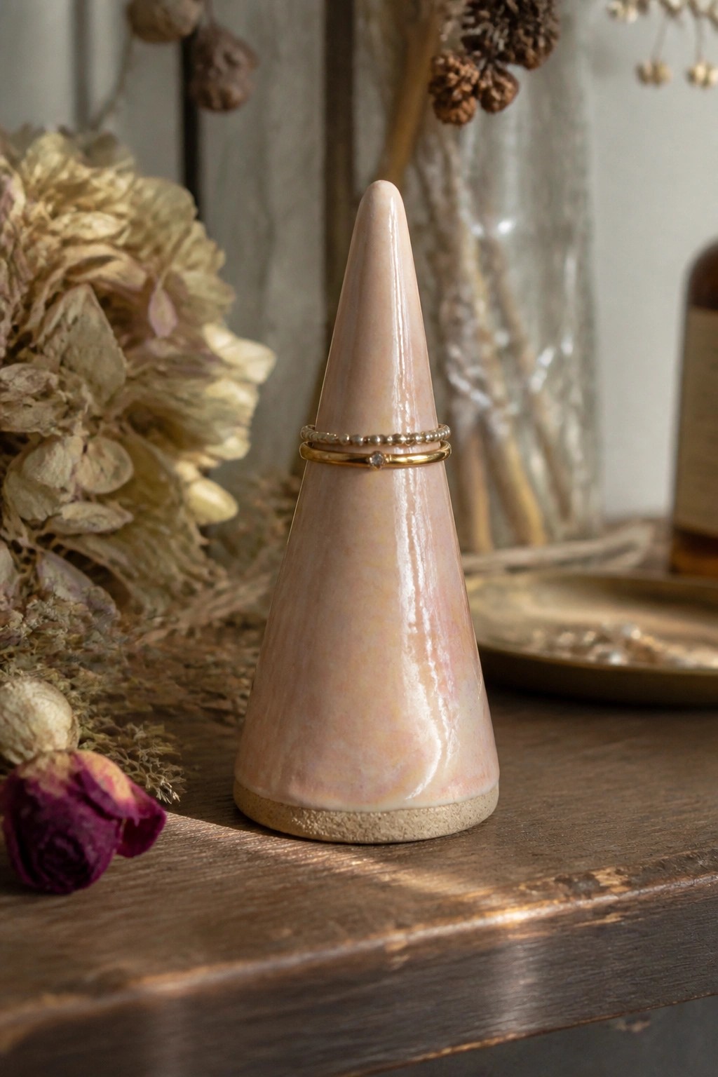 Pink ceramic cone ring holder with gold and beaded rings on wooden table