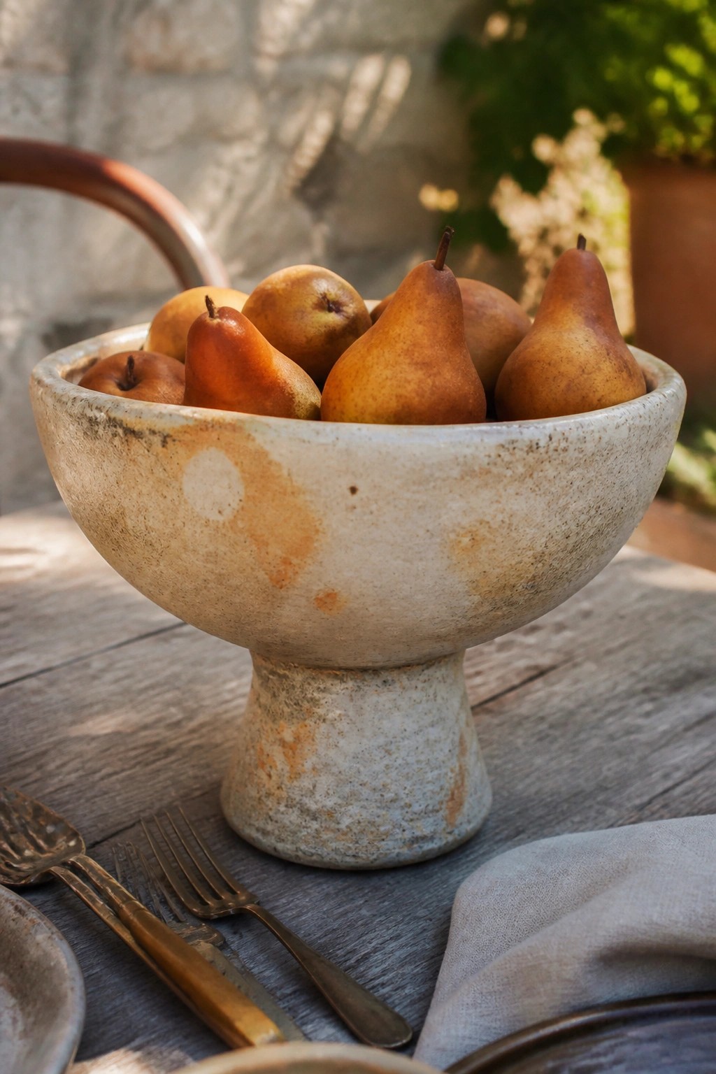 Rustic pedestal bowl of brown pears beside vintage forks on wooden table