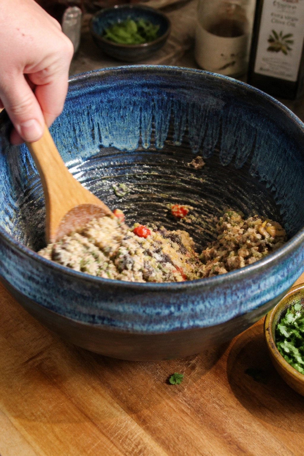 Hand stirring meat mixture in blue ceramic bowl with wooden spoon