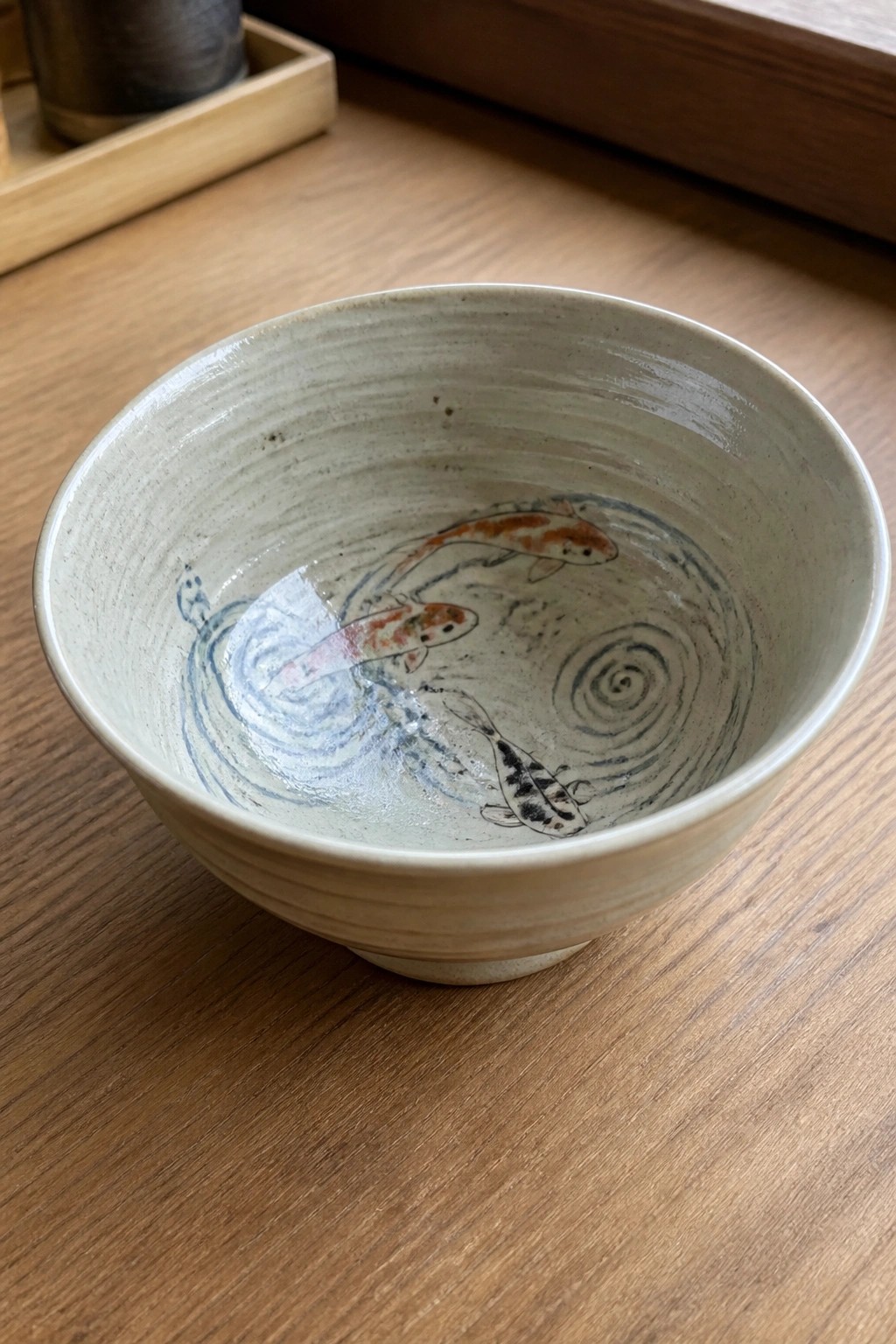 Rustic ceramic bowl with three colorful koi fish on wooden table