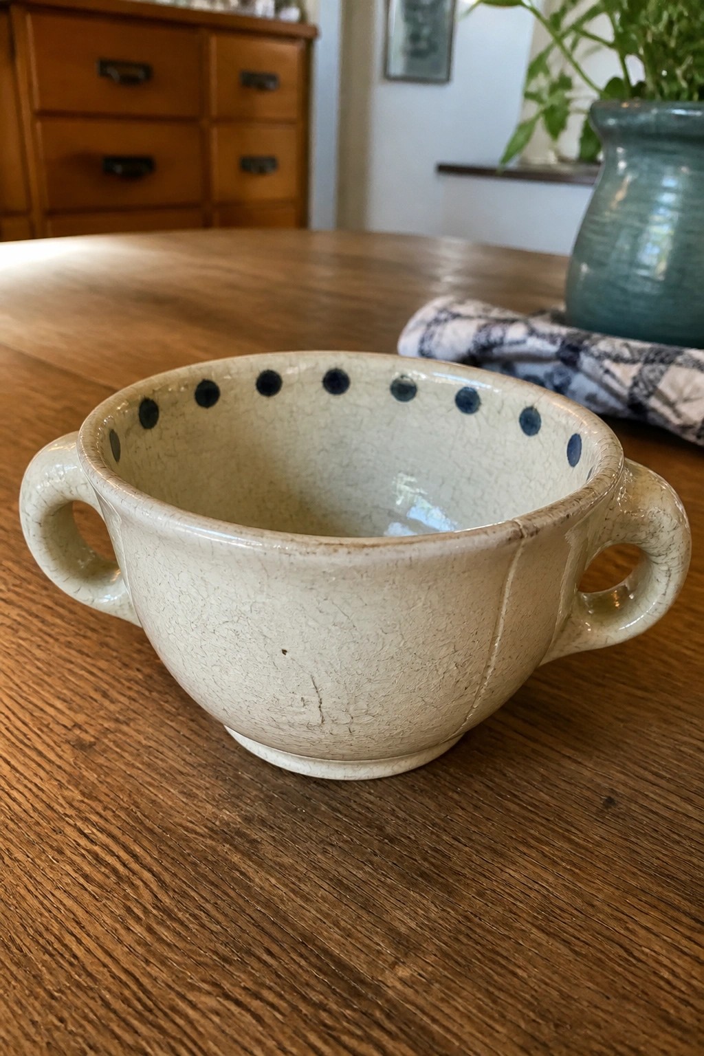 Cream ceramic bowl with blue rim dots and handles on wooden table