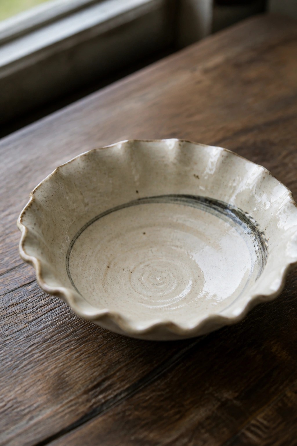 Handmade ceramic bowl with scalloped rim and dark spiral on wooden table