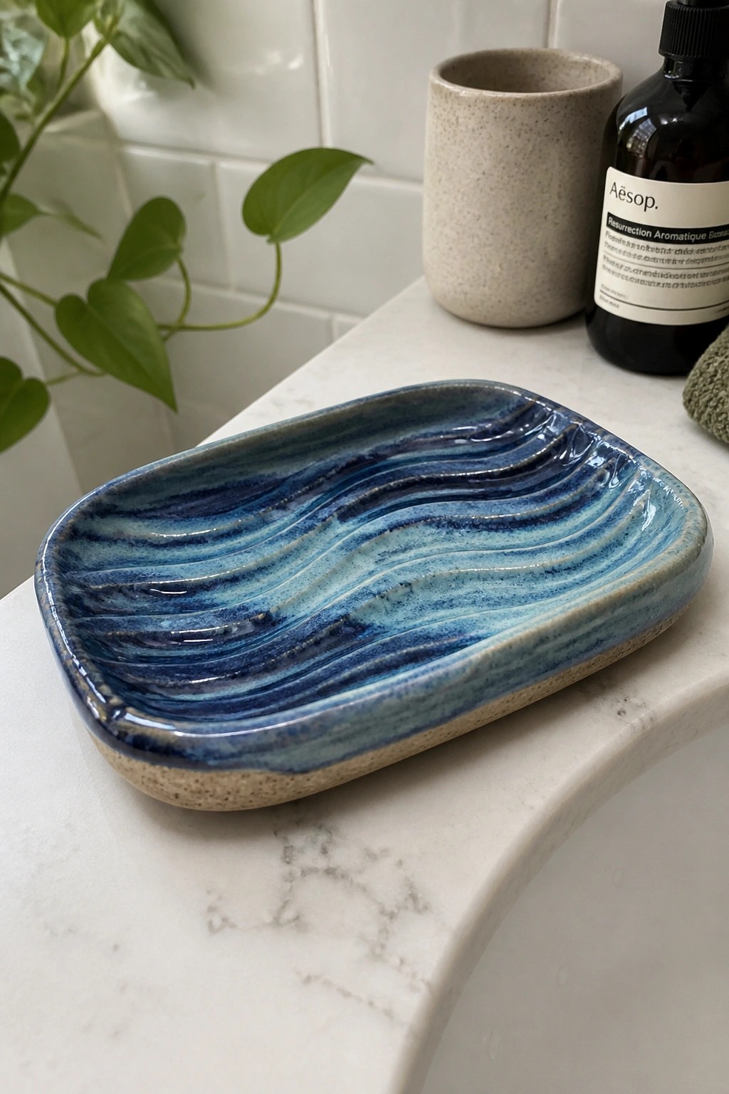 Blue wave-patterned ceramic dish on marble counter with plant and Aesop bottle