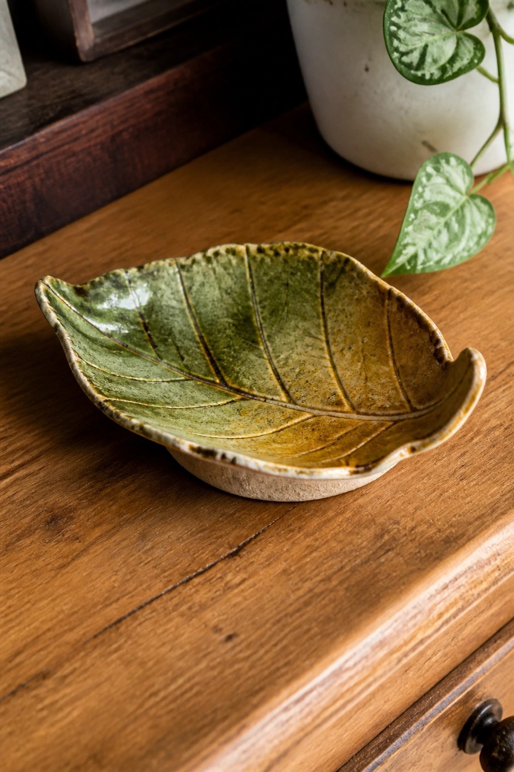 Green glazed ceramic leaf bowl on wooden table beside potted plant