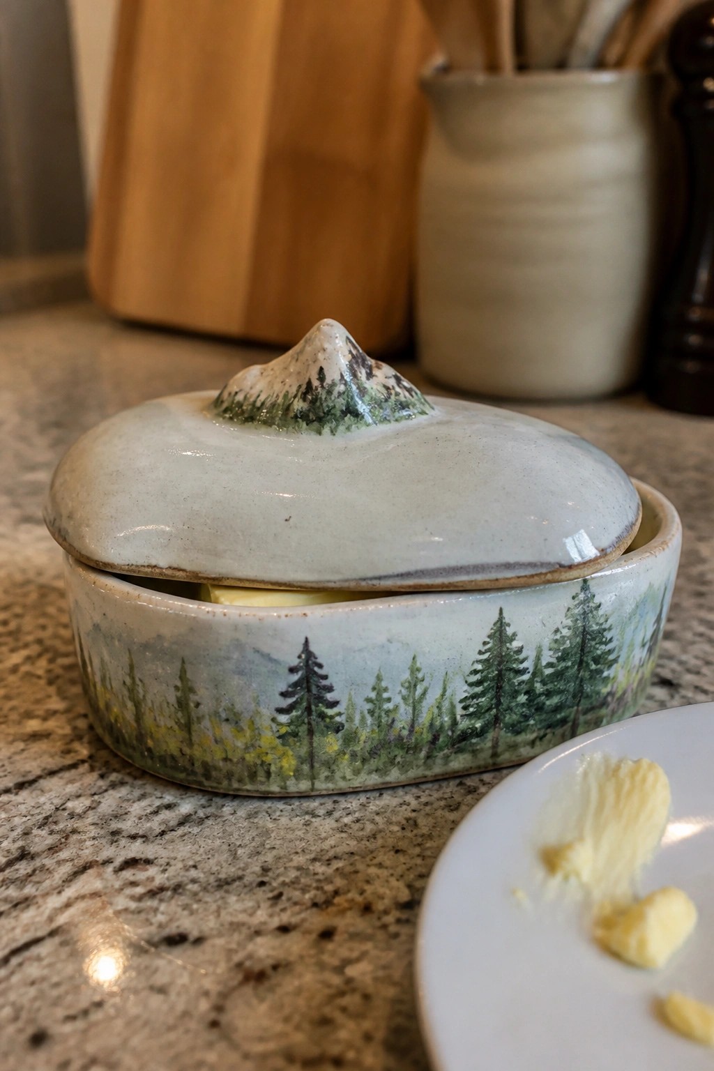 Ceramic butter dish with mountain lid and forest scene on granite counter