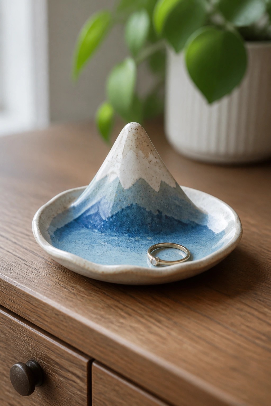 Blue ceramic mountain dish holding gold ring on wooden table with plant