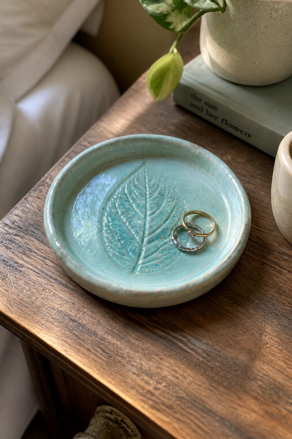 Turquoise ceramic dish with leaf imprint holding gold and silver rings on wood