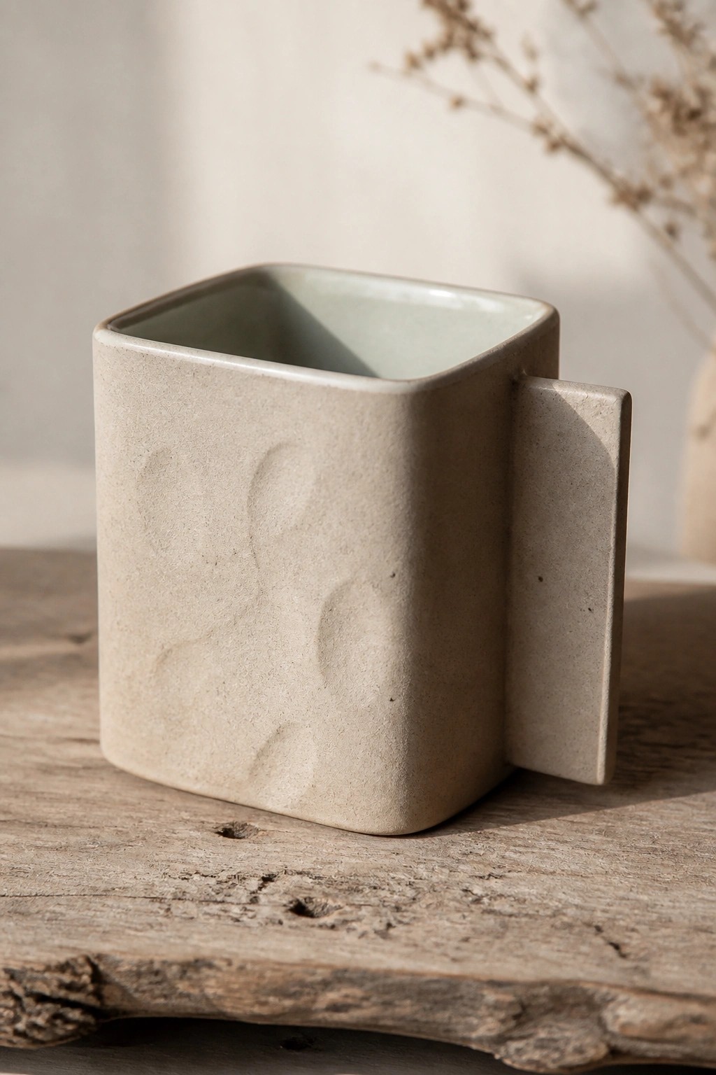 Square beige ceramic mug with textured indentations and handle on rustic wood.