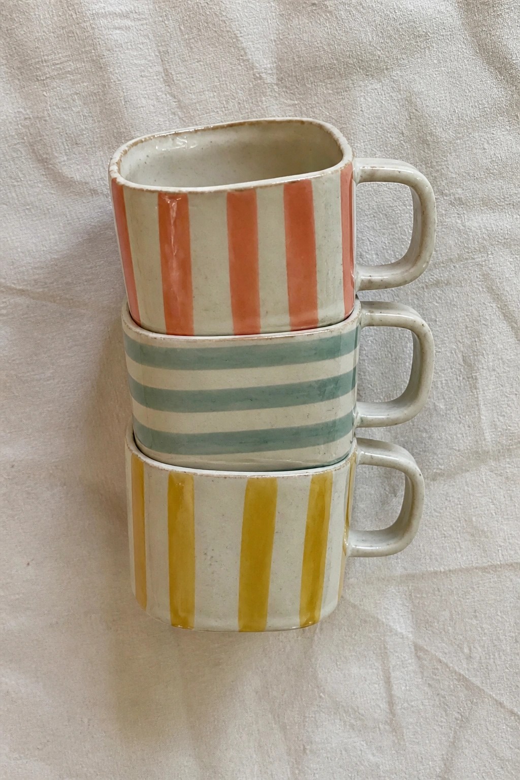 Three stacked ceramic mugs with orange, teal, and yellow vertical stripes.