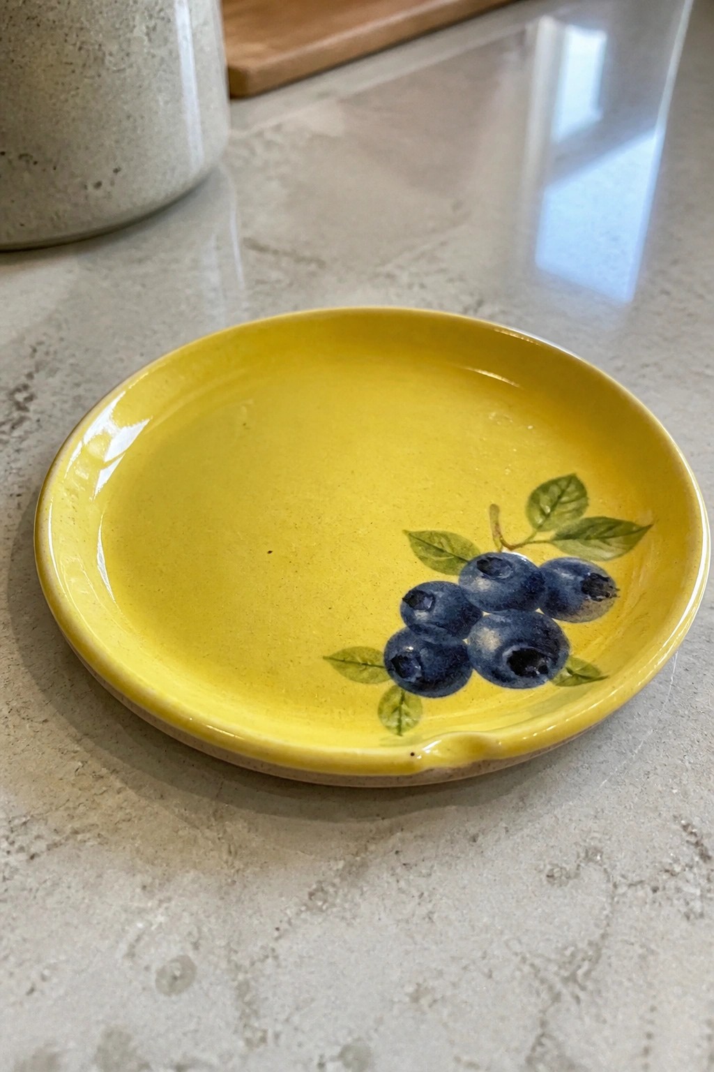 Yellow ceramic plate with blueberry and leaf design on marble countertop
