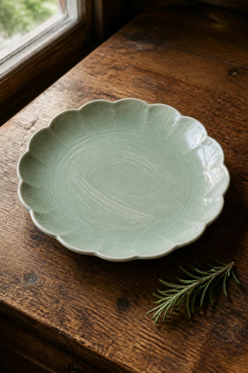 Light green scalloped ceramic plate on wooden table beside rosemary sprig