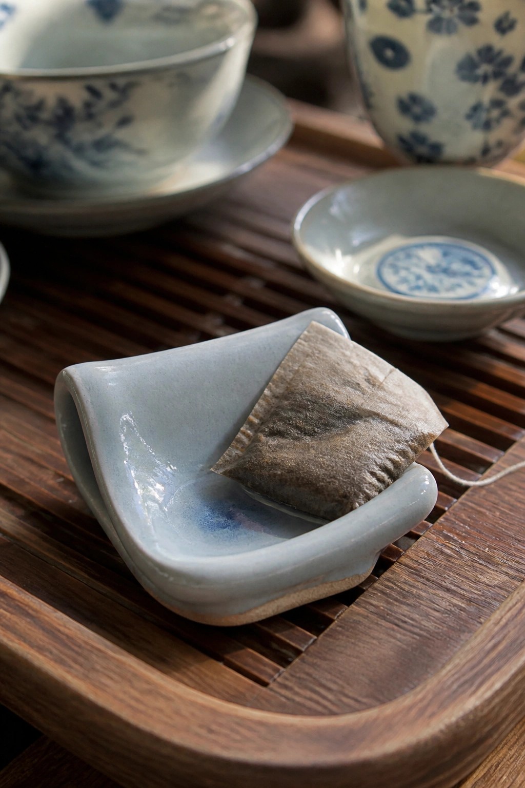 Light blue ceramic dish holding used tea bag on slatted wooden tray