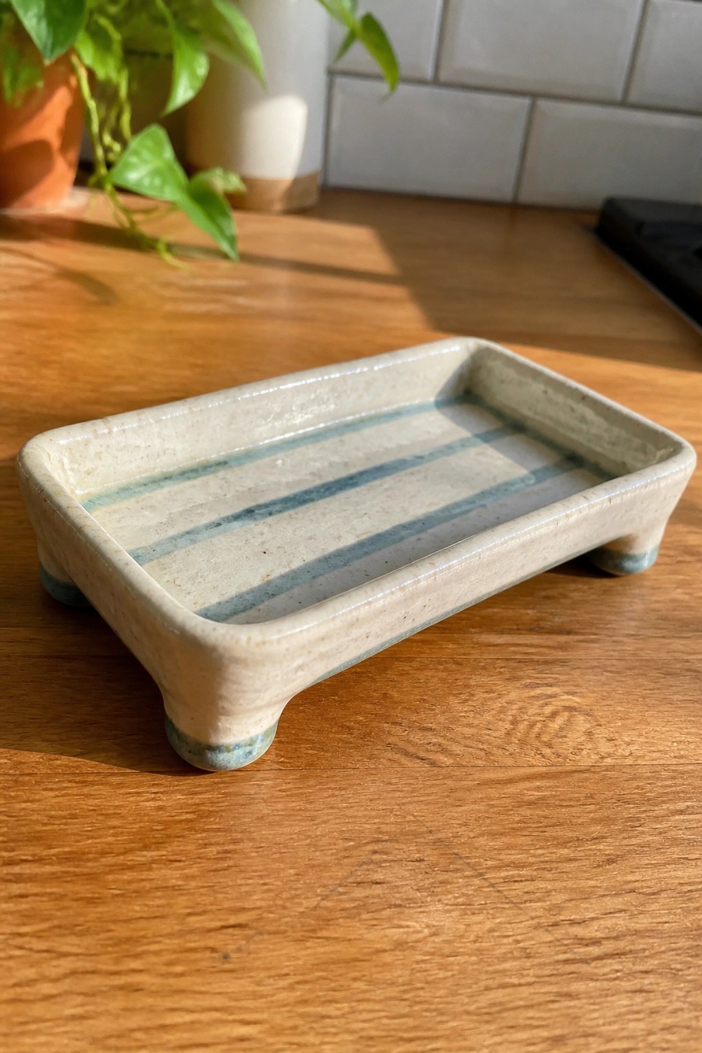 Rectangular beige ceramic tray with blue stripes on small feet atop wood