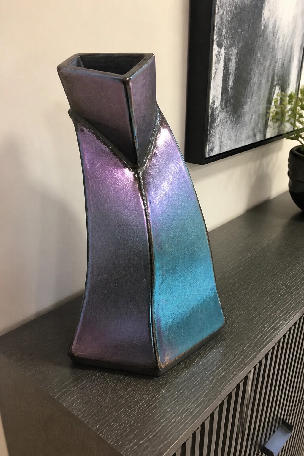 Iridescent angular vase in purple and blue tones on dark wooden surface
