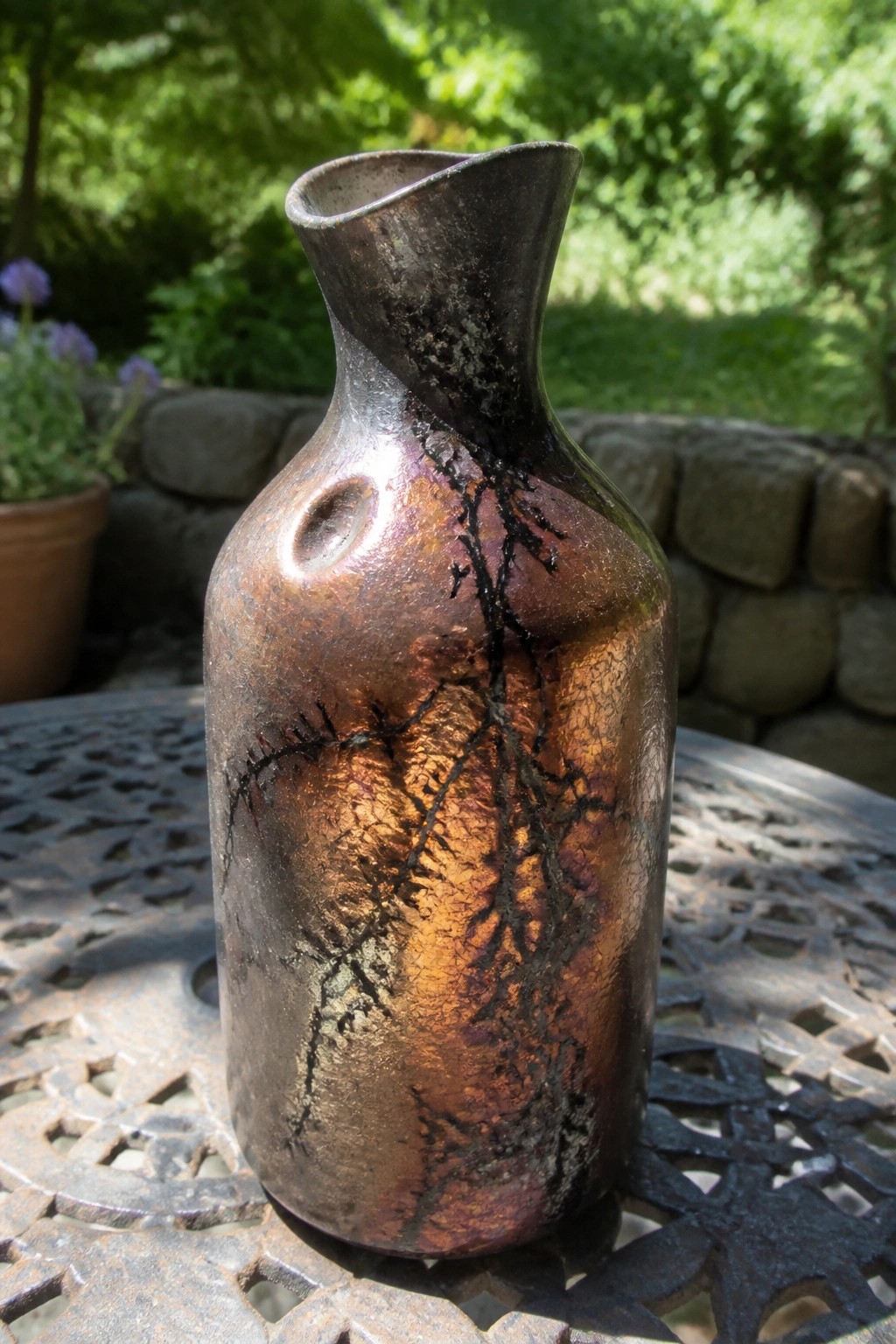 Iridescent crackled metallic vase with orange-brown tones on outdoor garden table