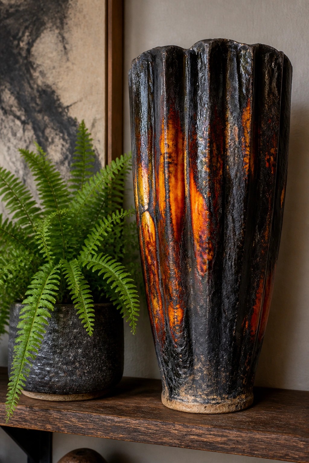 Fluted ceramic vase with black and orange glaze beside potted fern on shelf