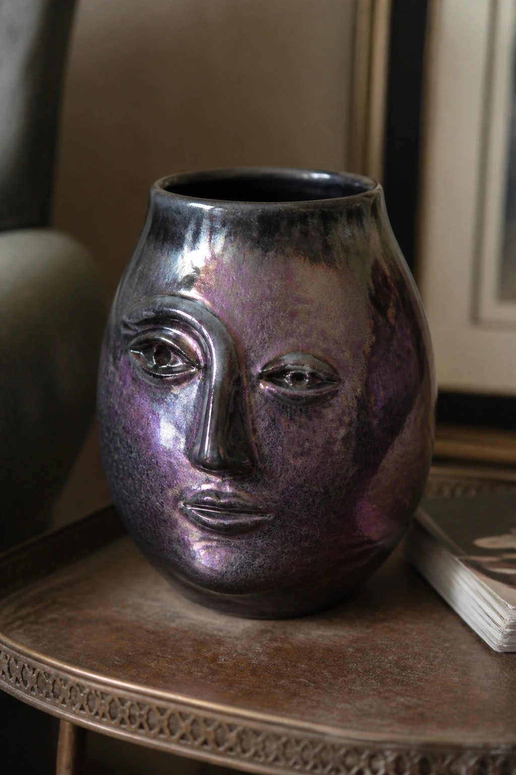 Iridescent purple metallic face vase on round wooden table beside book