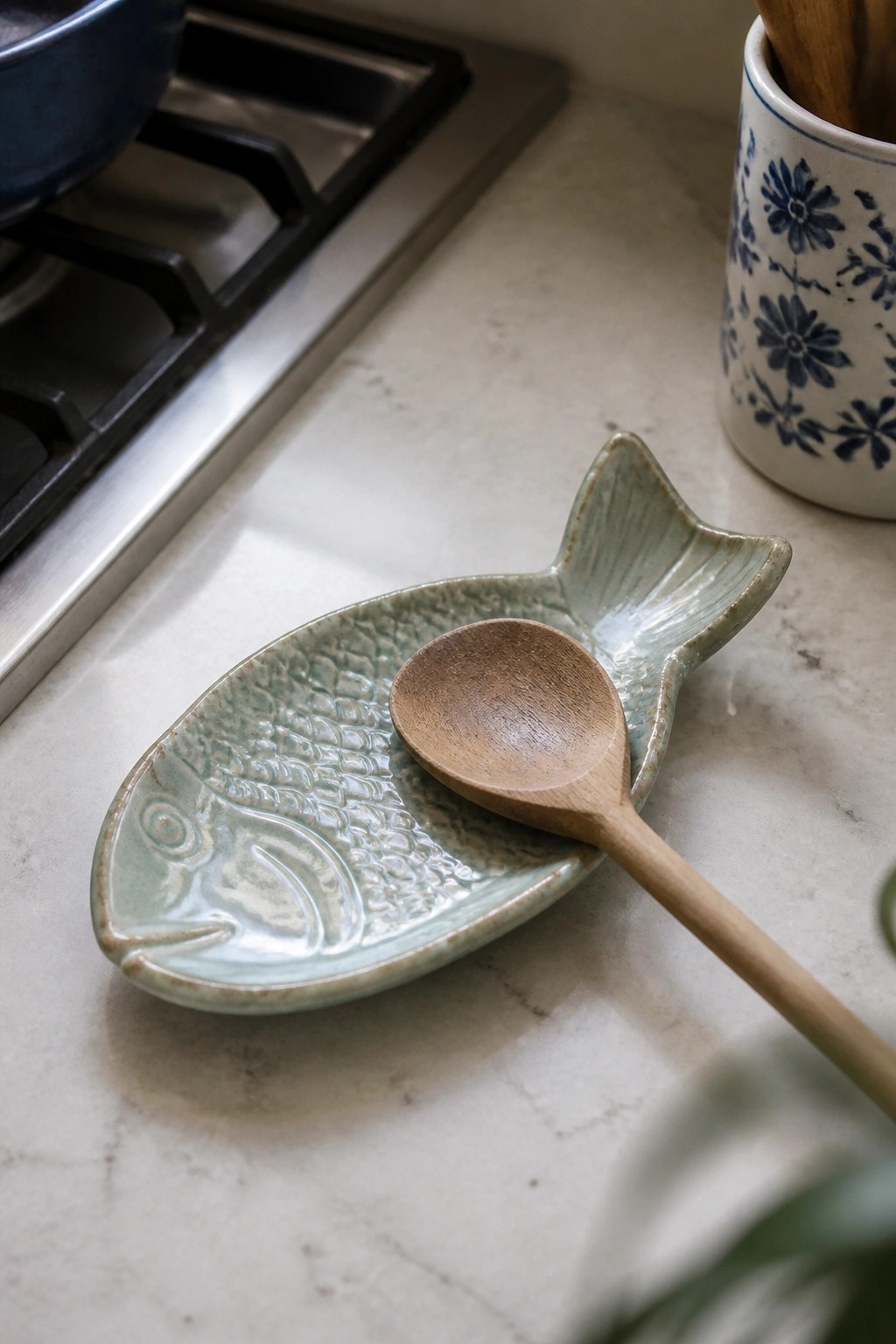 Wooden spoon resting on light green fish-shaped ceramic dish on marble counter