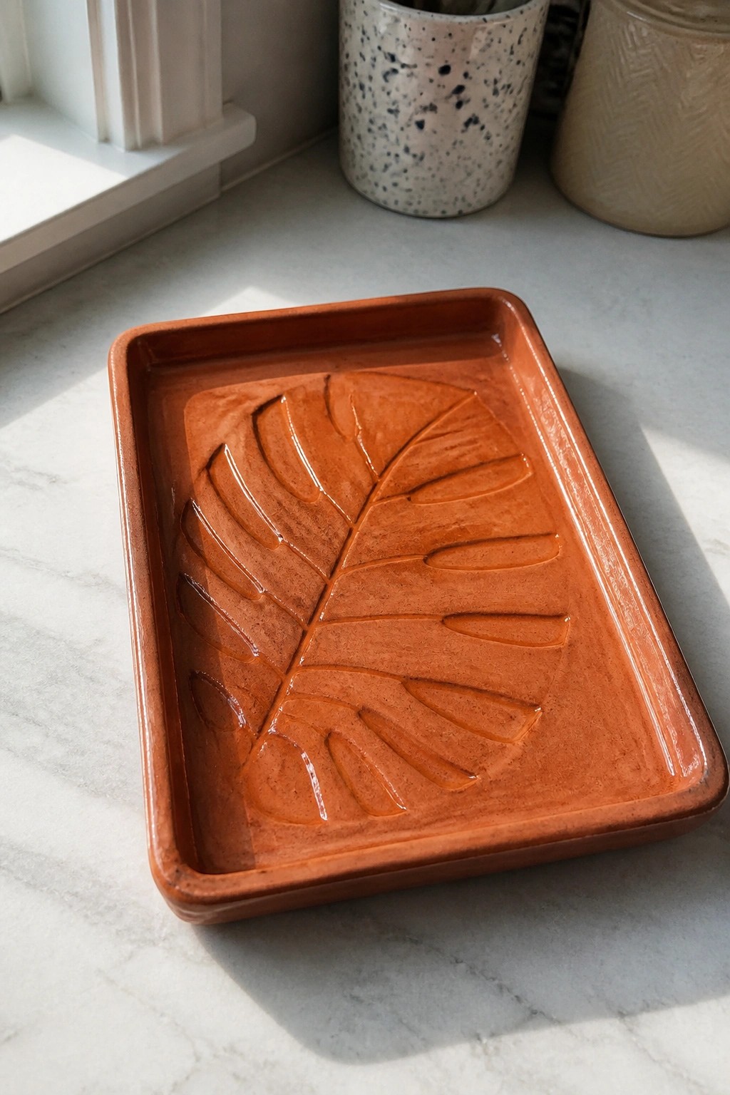Rectangular terracotta tray with embossed leaf design on white marble surface