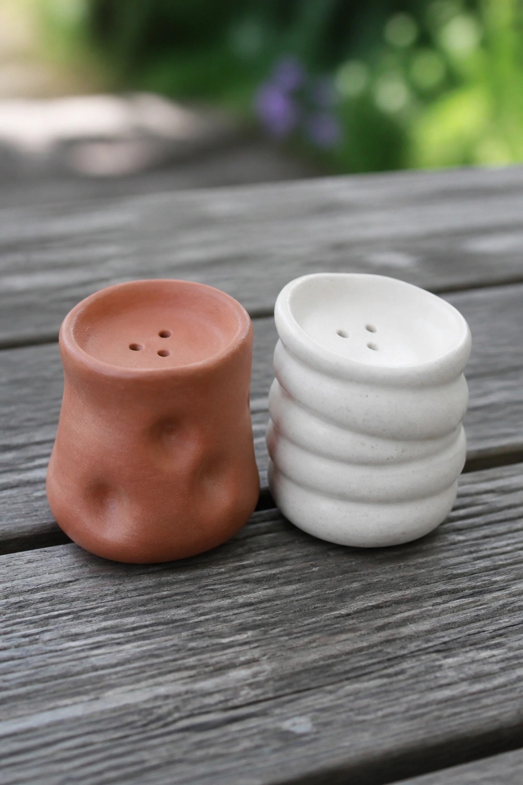 Terracotta and white ceramic shakers with holes on a wooden table