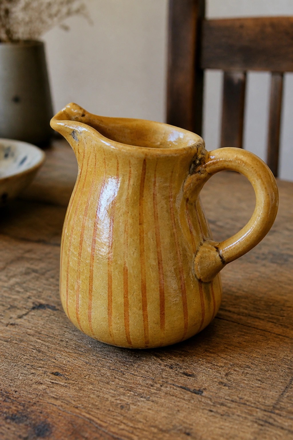 Yellow-brown striped ceramic pitcher with handle on rustic wooden table
