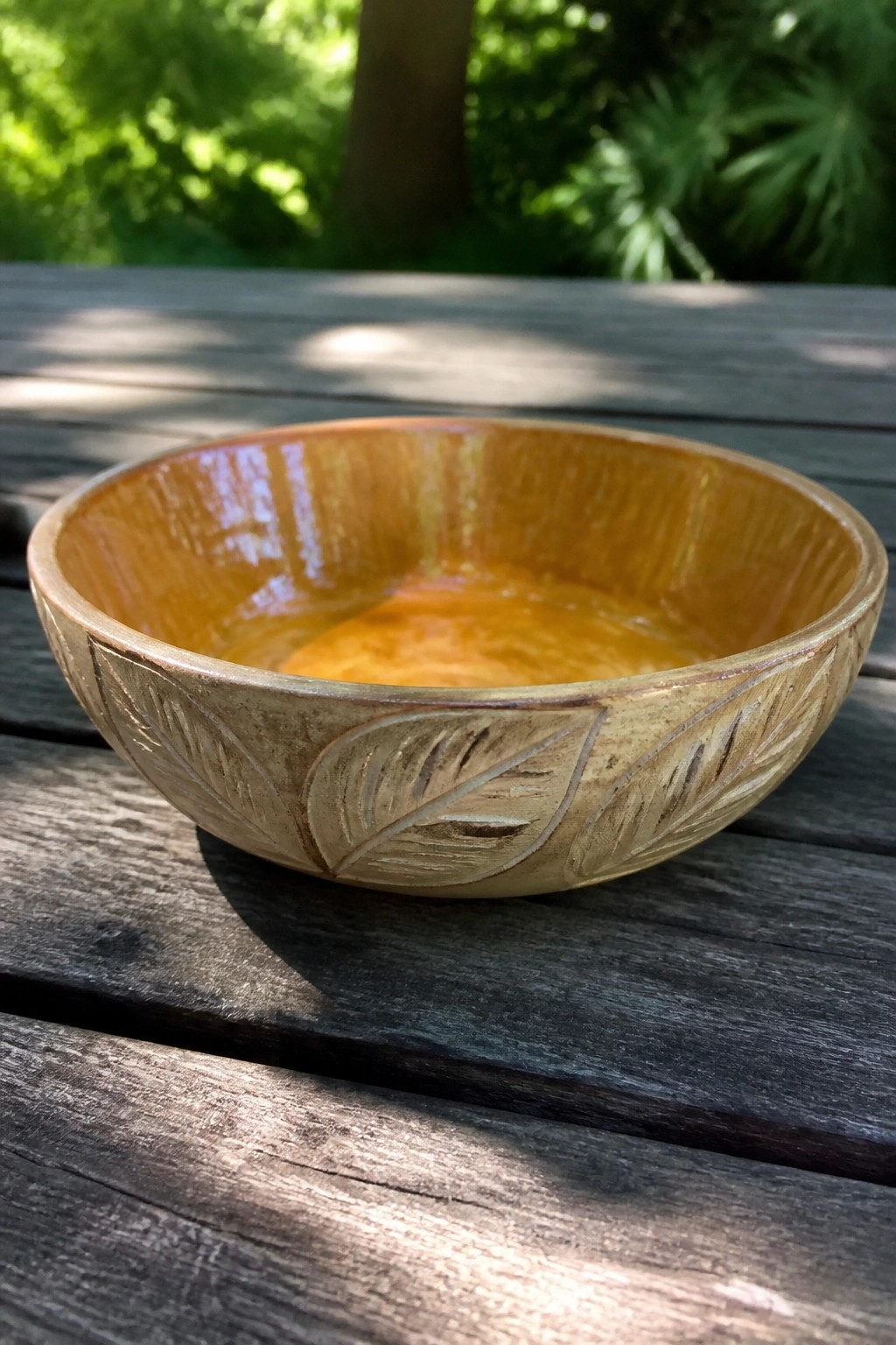 Amber-glazed ceramic bowl with leaf carvings on sunlit wooden table